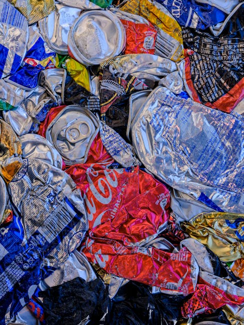 A collection of overflowing waste and recycling bins placed on a sidewalk in front of a commercial building, with various black, green, and red bins filled with mixed rubbish, paper, cardboard boxes, 
